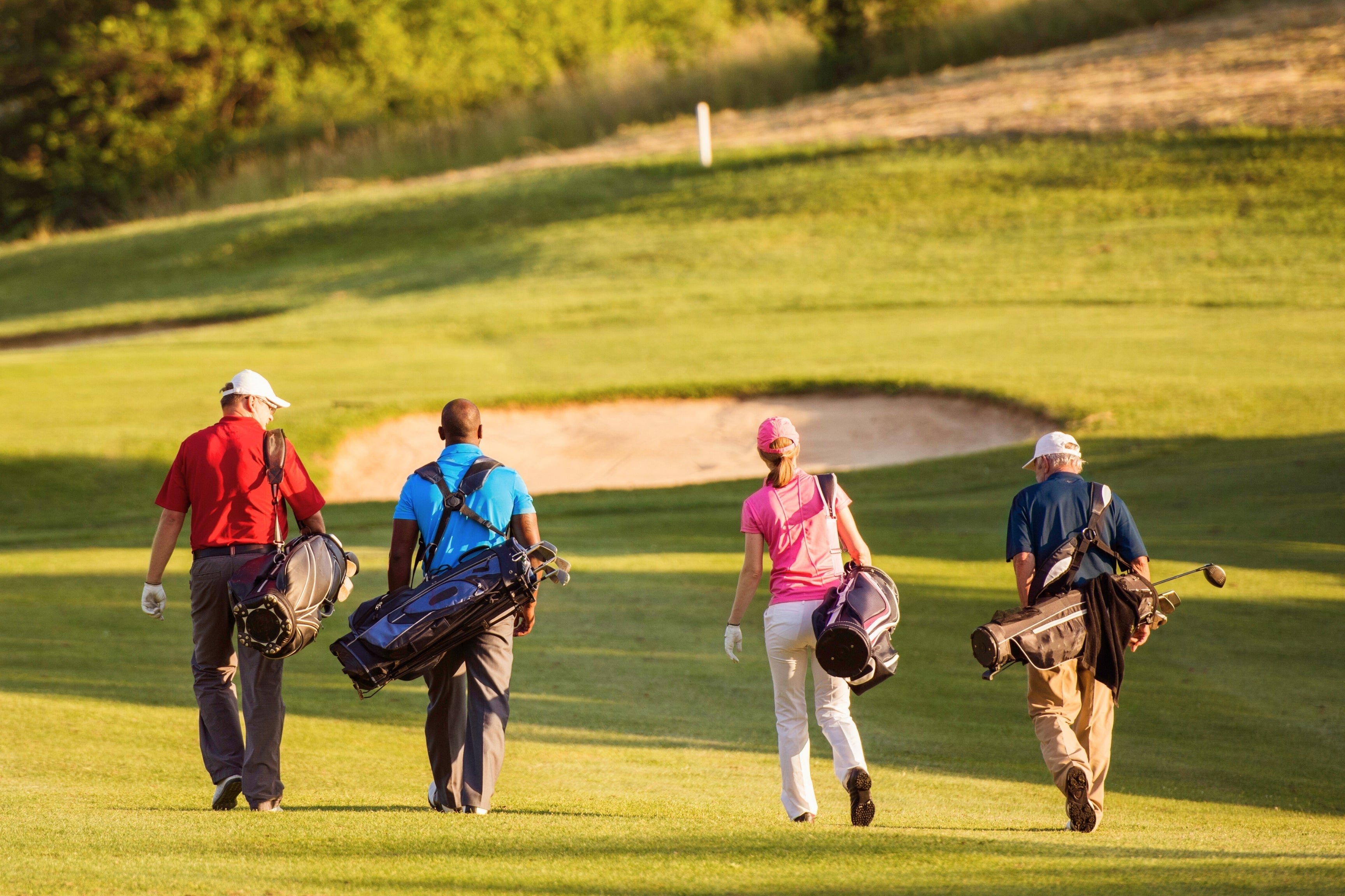 group of golfers carrying stand bags toward sand bunker on greens