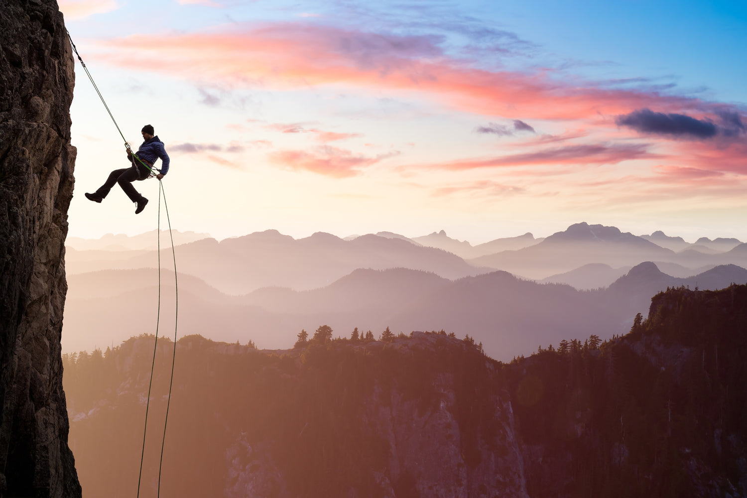 abseiling rappelling down cliff pink sky