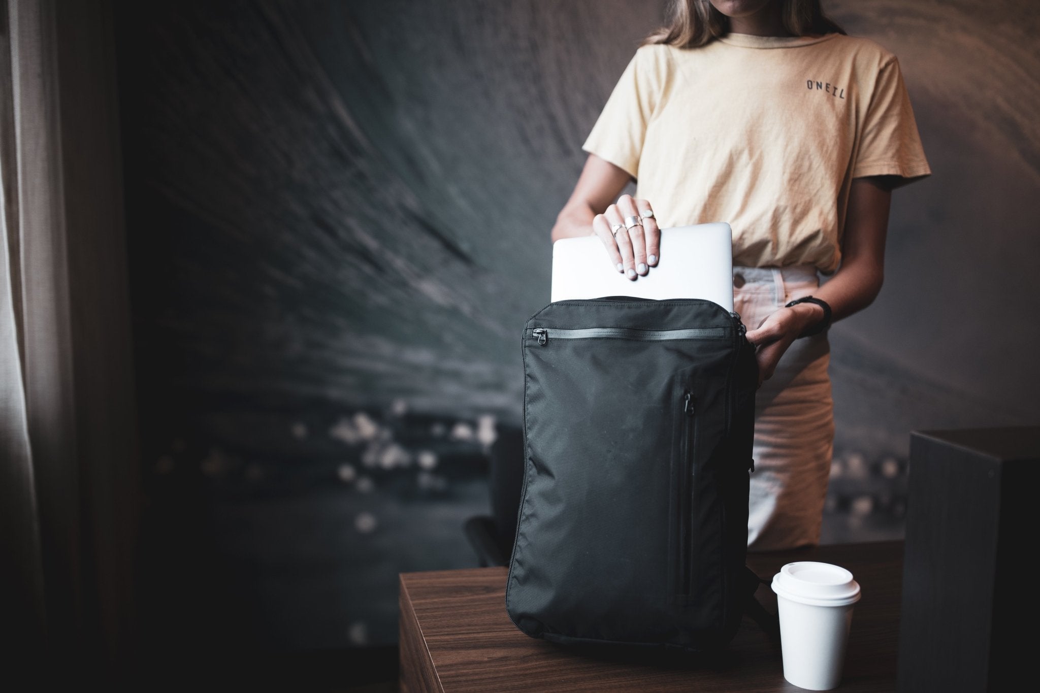 11L Day Bag - Gravel - Girl taking laptop out of 11 Liter backpack next to a table.