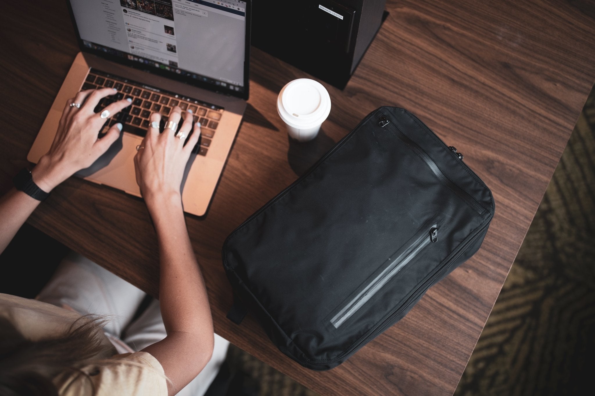 11L Day Bag - Gravel - 11 Liter Backpack closed on a table next to a girl on a laptop.