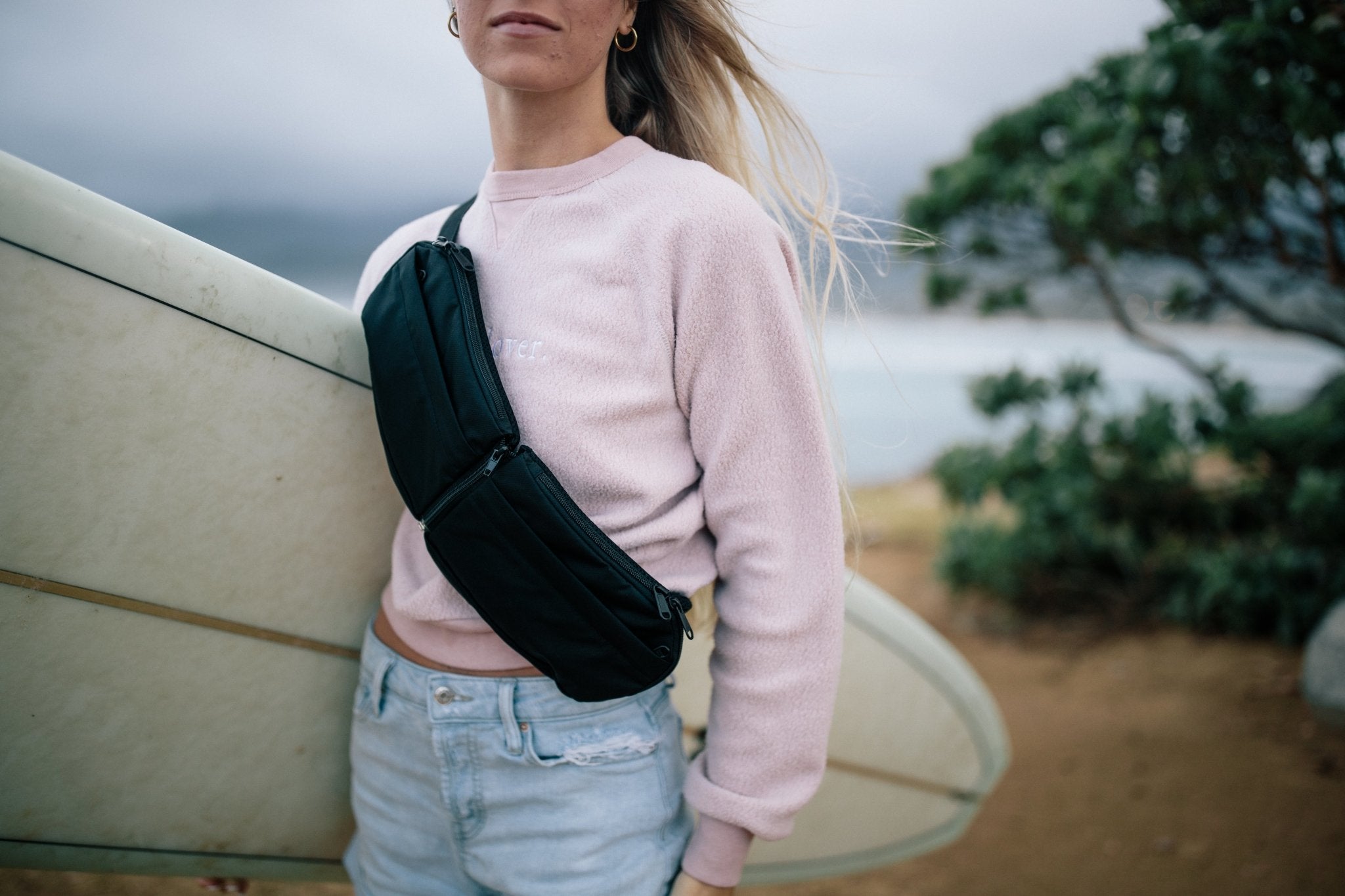 2L Sling Belt (42L Backpack Waist Belt/Sling Bag) - Gravel - Woman wearing 2 liter sling bag across chest holding a surfboard